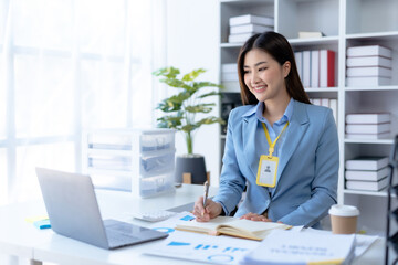 Charming Asian businesswoman working with a laptop at the office. Happy young Asian businesswoman sitting at desk and take notes with laptop computer in the office.