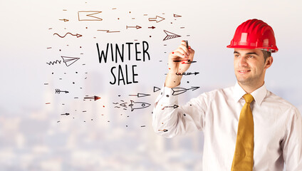 Young businessman with helmet drawing sale sign