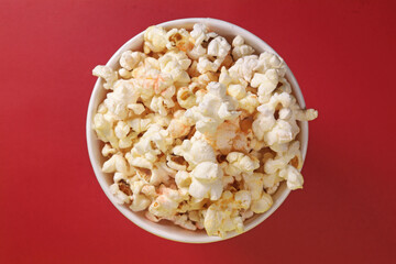 Paper cup with popcorn on red background, top view