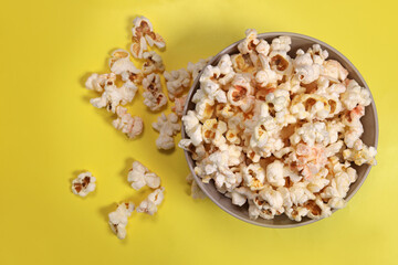 Paper cup with popcorn on yellow background, top view