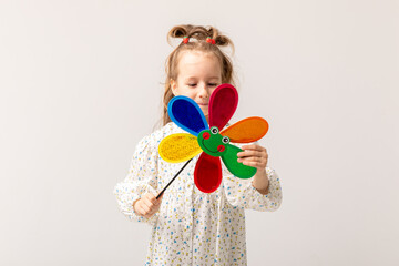 Photo of young cheerful girl in a beautiful white dress happy positive smile hold paper toy windmill on white background. Summer fashion for children.