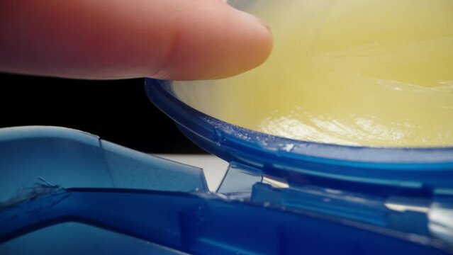 With my finger I take vaseline from a blue jar, on a black background. Dolly slider extreme close-up.