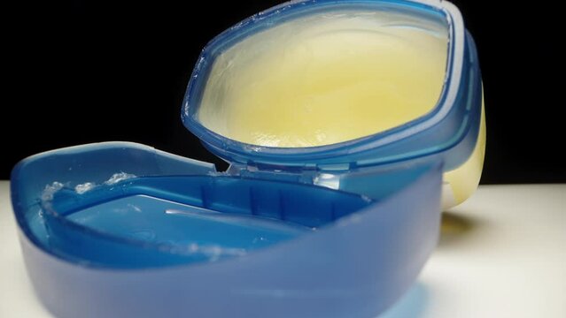 A blue jar with vaseline on a black background. I stick my fingers in there and lubricate them. Close up