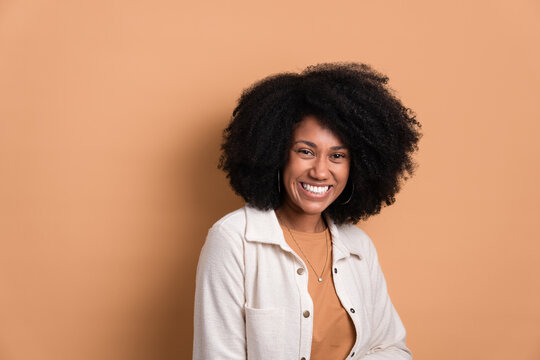 shy african american woman smiling and standing wearing white jacket in beige background. portrait, real people concept.