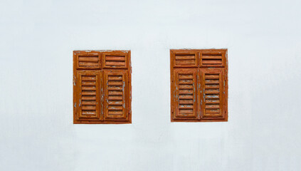 Brown wooden shutters ruined by time on a light gray wall of a house in the countryside in Europe.