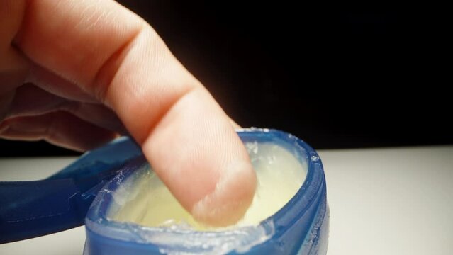 A blue jar of vaseline is on the table, I stick my finger in there and spread a little vaseline on it. Dolly slider close-up.