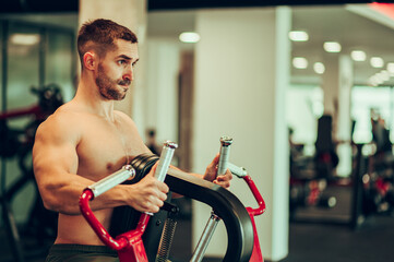 A strong shirtless sportsman is doing strength exercises on a chest pull machine.