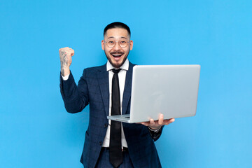 successful asian businessman in suit with laptop rejoice in victory over blue isolated background, korean entrepreneur