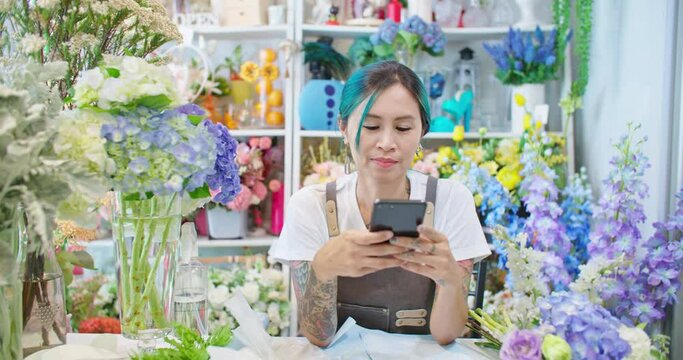 Asian female florist shop owner working with social media online store. Tattooed woman seller taking picture for customer and sending photo to client. E-commerce, SME entrepreneur, Small business.