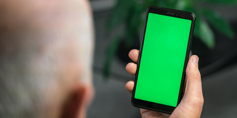 Male doctor holding in hands cell phone app mock up with green screen over shoulder view. Healthcare and telemedicine online consultation concept. Remote mobile medical application for smartphone.