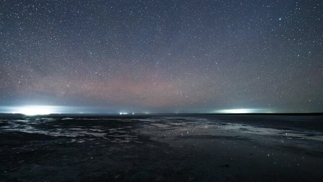 Night sky of stars and Milky way time lapse over the coastline of lake El'ton. Milky way Galaxy with stars and their reflection on water surface during an entire night.