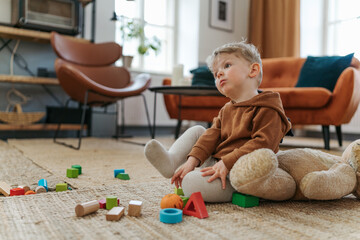 Little boy sitting on a carpet and playing with the cubes.