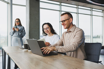 Workflow in an office with large windows, colleagues working on a new project using a portable laptop. Modern office with employees.