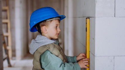 Little boy in unfinished house measuring wall in unfinished house with spirit level.