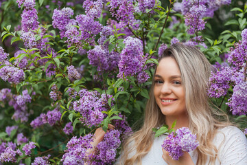 Portrait of beautiful young blue-eyed blonde woman near blooming lilac. Spring.