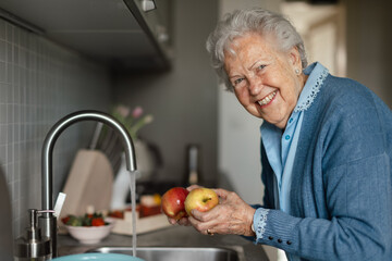 Happy senior woman washing apples in her kitchen.