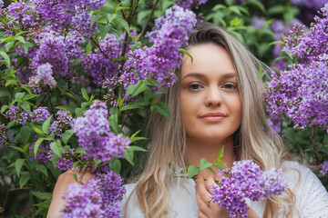 Portrait of beautiful young blue-eyed blonde woman near blooming lilac. Spring.