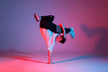 Foto op Plexiglas young guy dancer is dancing break in neon lighting, male acrobat is doing trick and dance exercise © Богдан Маліцький