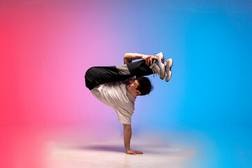 dancer doing acrobatic trick and dancing breakdance in neon red and blue lighting, young guy stands...