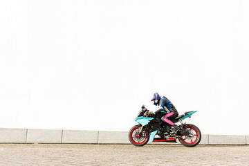 guy motorcyclist in professional protective equipment and helmet rides sports fast motorcycle against white wall