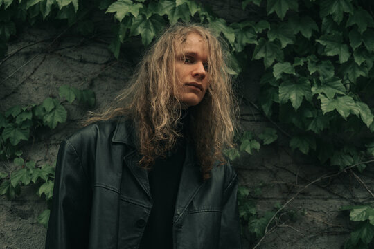 Young male model brutal man wearing blond long hair and black clothes on city street