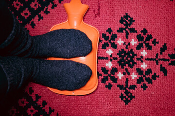 Person warming feet with  Rubber heating pad on a red carpet background, old fashion style