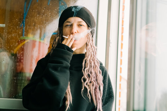 Female wearing hat smoking self-roll weed cigarette blowing smoke