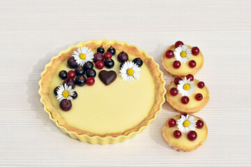 Shortbread vanilla tartlets with fruits, chocolate heart and edible daisy flowers, light background