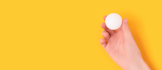 Banner with female hand hold white ball for ping pong on a yellow background. Composition with copy...