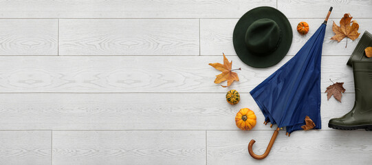 Umbrella, rubber boots, hat and autumn decor on light wooden background with space for text