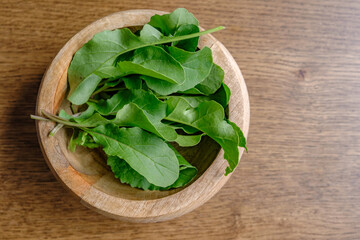 close up of arugula in a bowl with a walnut wood background