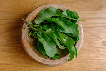 close up of arugula in a bowl with a walnut wood background