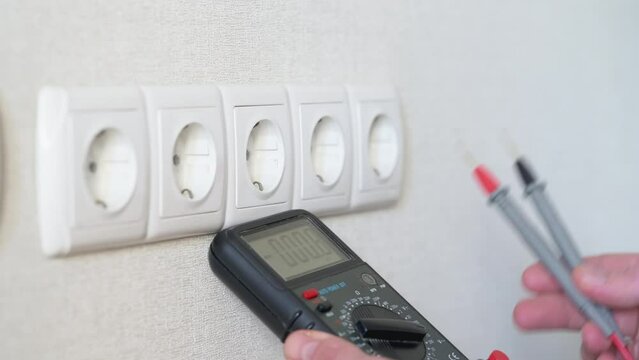 Electrician checking socket voltage with digital multimeter