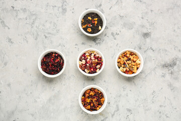 Bowls with different dried fruit tea on grey grunge table