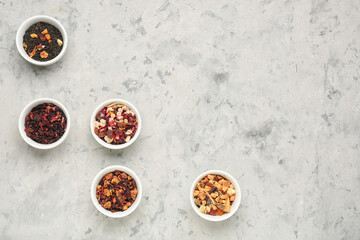 Bowls with different dried fruit tea on grey grunge table