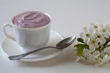On the table are a mug of yogurt and a white flower. On a white background.