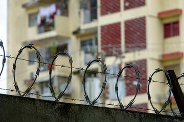 Barbed wire on concrete wall and tall residential building in background