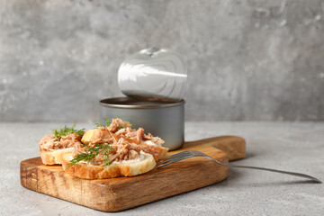 Board with delicious tuna bruschettas and tin can on grey table