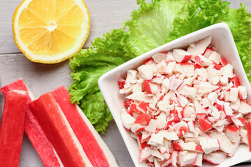 Bowl with tasty chopped crab sticks on light wooden background, closeup © Pixel-Shot
