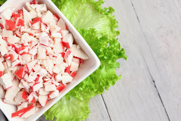 Bowl with tasty chopped crab sticks on light wooden background, closeup © Pixel-Shot