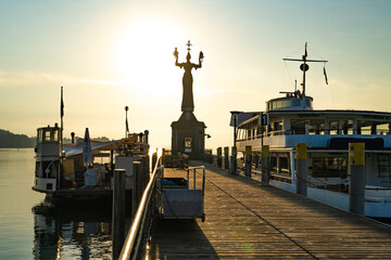 Beautiful sunrise view from wooden pier on Imperia statue at harbor entrance and Lake Constance in early morning hours. Steamer harbor, Constance, Baden-Württemberg, Germany, Europe.
