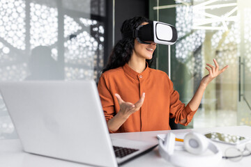 Successful latin american woman in office using vr glasses for video call and chatting online in virtual reality simulator, online conference with colleagues remote in metaverse.