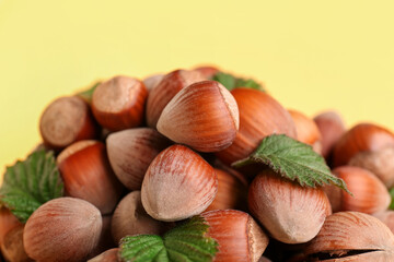 Shelled hazelnuts with leaves on yellow background, closeup