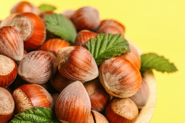 Shelled hazelnuts with leaves on yellow background, closeup