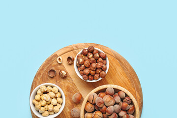 Board and bowls with hazelnuts on blue background