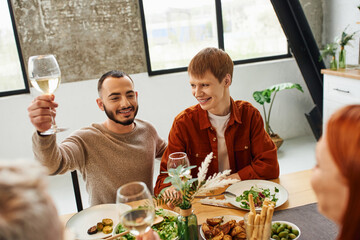 bearded man toasting with wine near happy gay partner and delicious family dinner in modern kitchen.