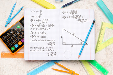 Copybook with maths formulas, calculator and stationery on white grunge background