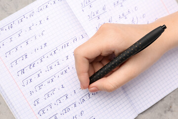 Woman writing maths formulas in copybook with pen, closeup