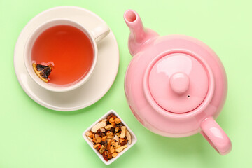 Ceramic teapot with cup of fruit tea on green background
