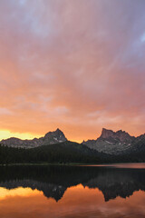 Fototapeta premium Golden sunset in mountain lake. Two peaks reflected in water